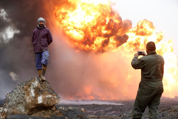 Мужчина фотографирует своего друга на фоне горящих нефтяных скважин, подожженных боевиками ИГ в Кайяре, Ирак