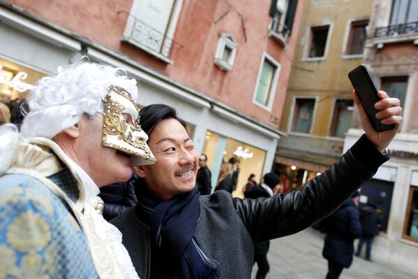 Турист делает селфи с участником маскарада во время Венецианского фестиваля