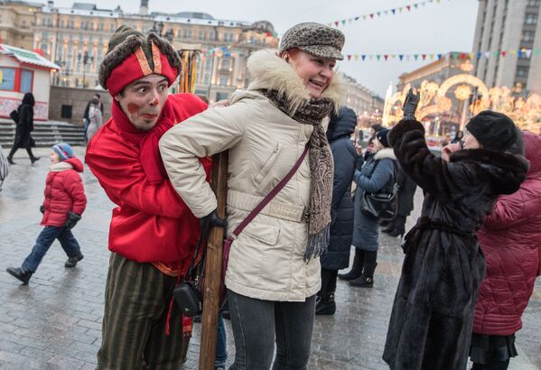Участник анимационной программы, одетый в праздничный костюм, и гости праздника во время открытия фестиваля Московская масленица на Манежной площади