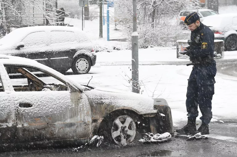 Полицейский осматривает сожженный автомобиль в результате беспорядков пригороде Стокгольма Полицейский осматривает сожженный автомобиль в результате беспорядков пригороде Стокгольма