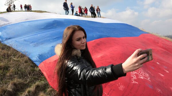Девушка делает селфи на фоне огромного флага России на фестивале Крымская весна в селе Мирное Симферопольского района Республики Крым