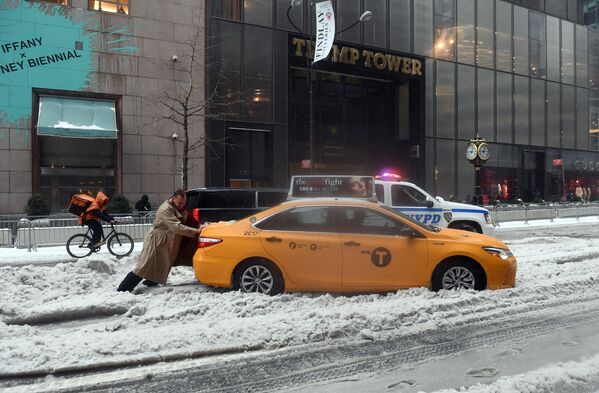 Пассажир толкает такси, застрявшее в снегу в результате снегопада в Нью-Йорке