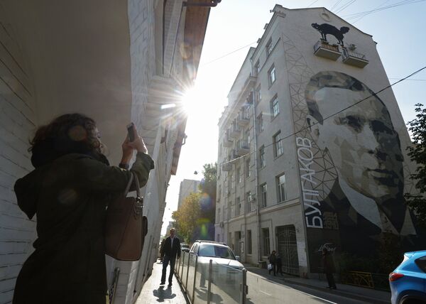 Женщина фотографирует портрет писателя Михаила Булгакова, изображенный на стене дома в Большом Афанасьевском переулке в Москве