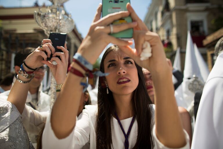 Женщина фотографирует шествие братства Ла-Пас во время Страстной недели в Севилье, на юге Испании