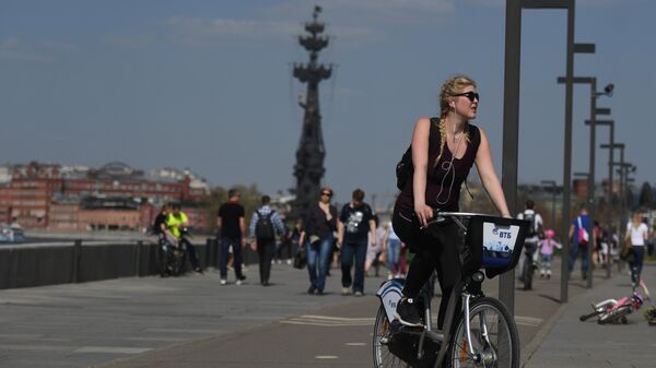 Девушка на велосипеде из городского общественного проката на набережной Парка искусств Музеон