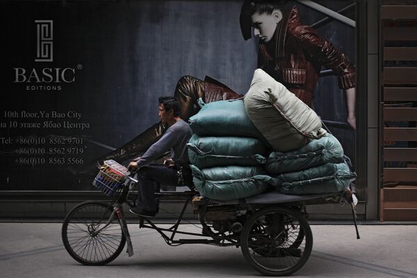Житель Пекина на трехколесном велосипеде, нагруженном товарами, проезжает мимо Международного торгового центра Житань