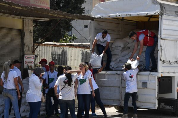 Представители Сирийского арабского красного полумесяца и Дамаскской молодежной волонтерской команды разгружают грузовик с гуманитарной помощью для жителей квартала Кабун в пригороде Дамаска