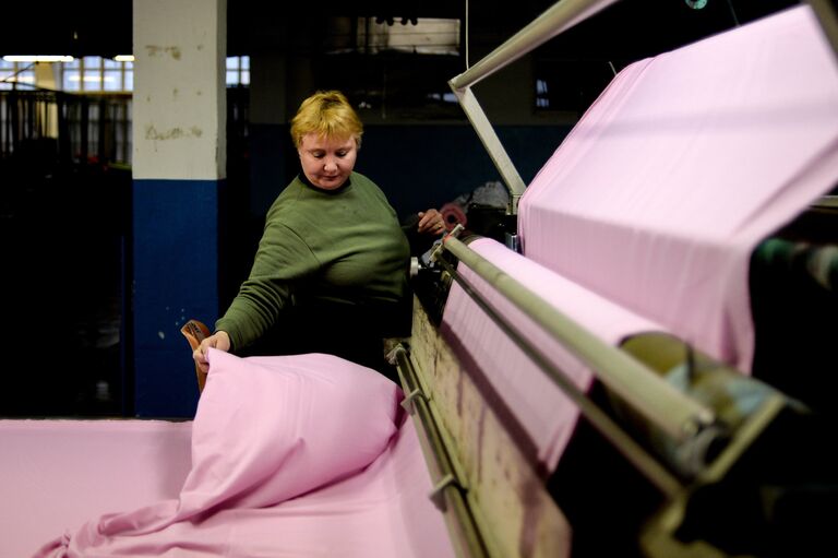 Сотрудница трикотажной фабрики выполняет операцию настелания полотна в закройном цехе