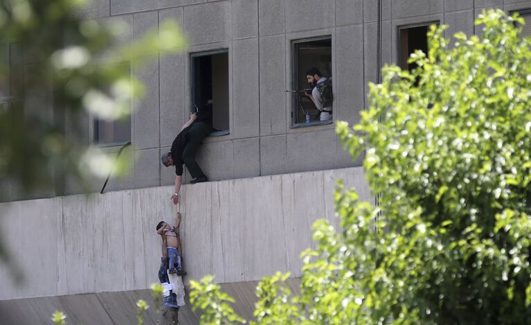 Человек передает ребенка охраннику из окна здания парламента Ирана в Тегеране. 7 июня 2017 года