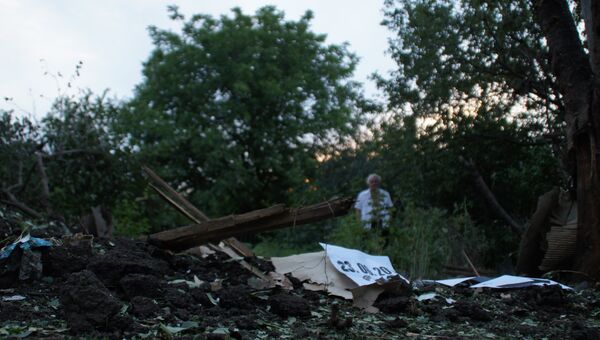 Местный житель стоит у воронки от снаряда во дворе соседского дома в Донбассе. Архивное фото