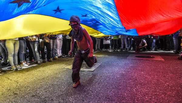 Мальчик пробегает под флагом Венесуэлы во время протестов в Каракасе. Архивное фото