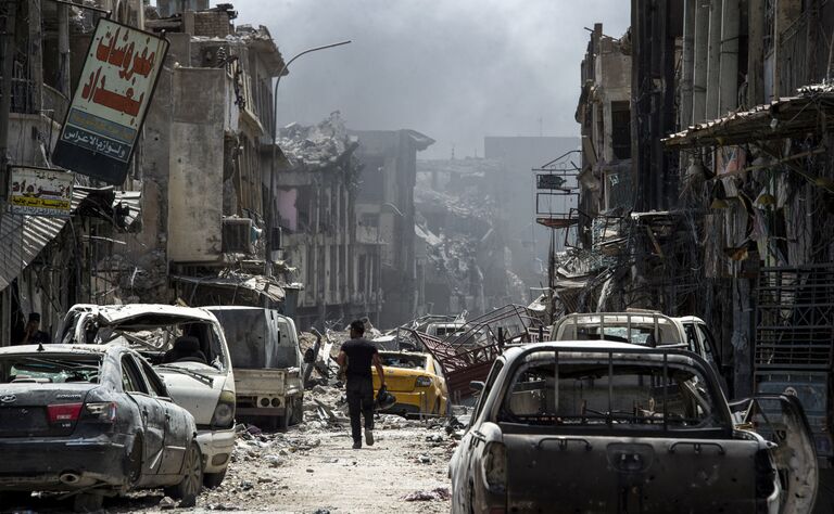 Мужчина идет вдоль сгоревших автомобилей в Мосуле Мужчина идет вдоль сгоревших автомобилей в Мосуле