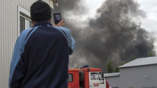 Мужчина снимает на телефон как пожарный вертолет МЧС РФ тушит возгорание в ангаре с лакокрасочной продукцией в Колпинском районе Петербурга