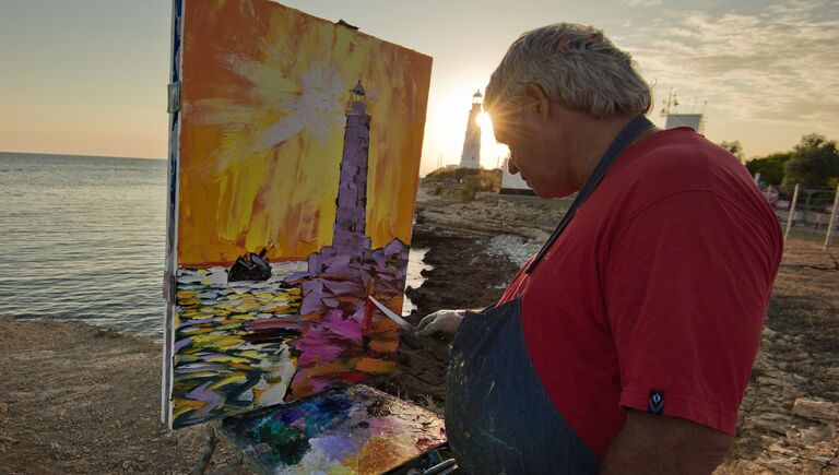 Художник пишет картину на берегу Черного моря вблизи маяка на мысе Тарханкут в Крыму