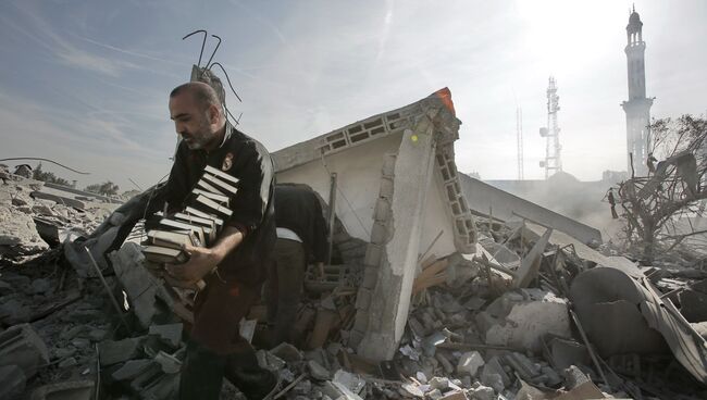 Мужчина выносит стопки Корана из разрушенного взрывом здания в Газе. Архивное фото
