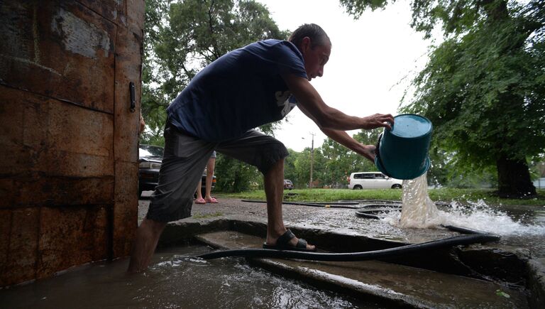 Мужчина вычерпывает воду из подъезда на затопленной улице Уссурийска. 7 августа 2017