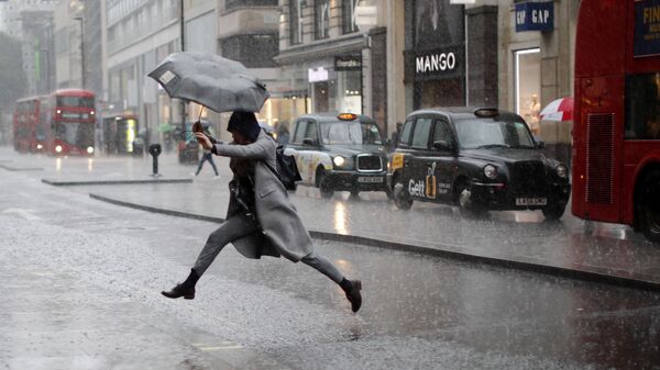 Девушка перепрыгивает лужу во время дождя в Лондоне. Архивное фото