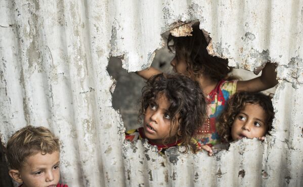 Палестинские дети смотрят на улицу через отверстие в заборе в Газе