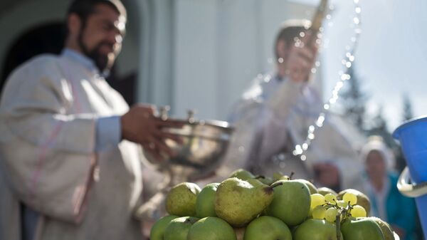 Священнослужитель окропляет святой водой яблоки и фрукты во время богослужения в честь праздника Преображения Господня у собора Воздвижения Креста Господня в Омске. 19 августа 2017