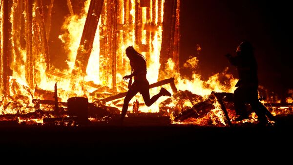 Мужчина пытается пробежать сквозь пламя, игнорируя пожарных, на фестивале Burning Man в пустыне Невада, США. 2 сентября 2017