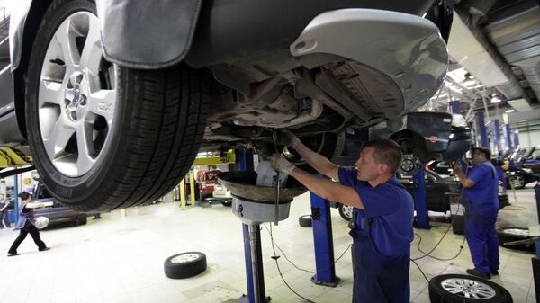 Сотрудник цеха слесарного ремонта проводит замену масла в двигателе автомобиля