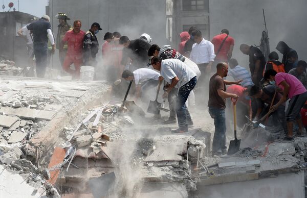 Люди помогают извлекать пострадавших из под обломков здания после землетрясения в Мехико