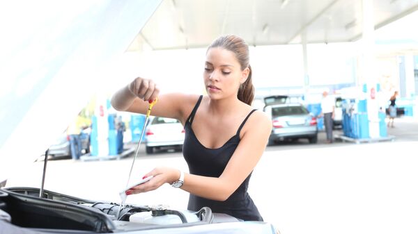 Девушка замеряет уровень масла в двигателе автомобиля