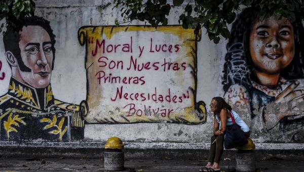 Женщина сидит около стены с граффити с цитатой Симона Боливара Мораль и просвещение - наша насущная необходимость напротив избирательного участка в Каракасе
