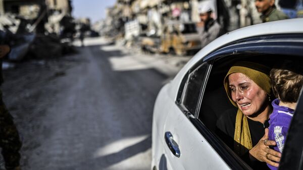 Женщина с ребенком плачет, глядя на свой дом в Ракке, Сирия