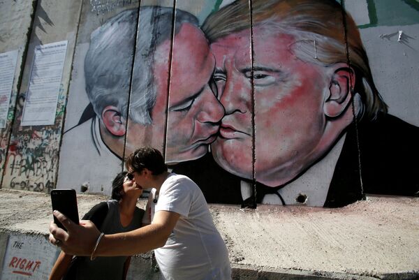 Пара целуется на фоне граффити с изображением поцелуя израильского премьер-министр Биньямина Нетаньяху и президента США Дональда Трампа. Вифлеем, Палестина