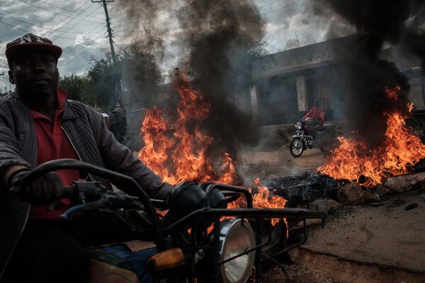 Водители мототакси проезжают мимо горящих баррикад во время протеста в Маенго, Кения