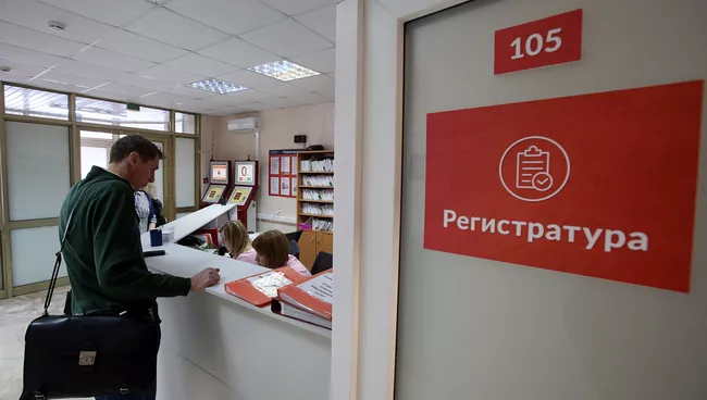 Посетитель у регистрационного стола в поликлинике. Архивное фото