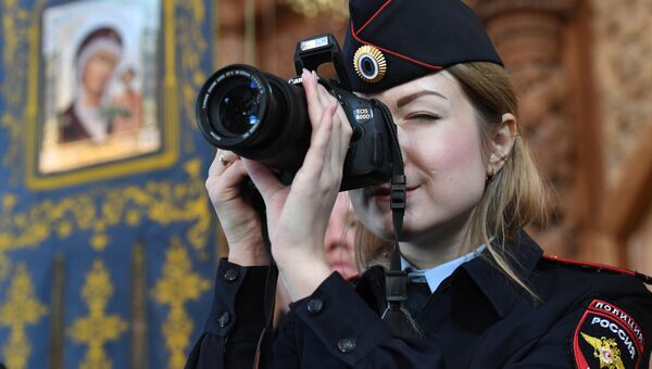 Сотрудник полиции фотографирует во время Божественной литургии в кафедральном соборе Успения Пресвятой Богородицы в Астрахане
