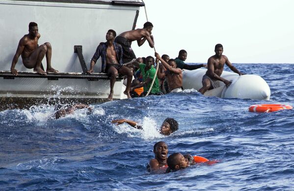 Мигранты с затонувшей лодки возле лодки береговой охраны Ливии во время спасательной операции