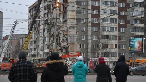 Прохожие наблюдают за ходом работ служб МЧС РФ по расчистке завалов частично обрушившегося жилого панельного дома на Удмуртской улице в Ижевске. 10 ноября 2017