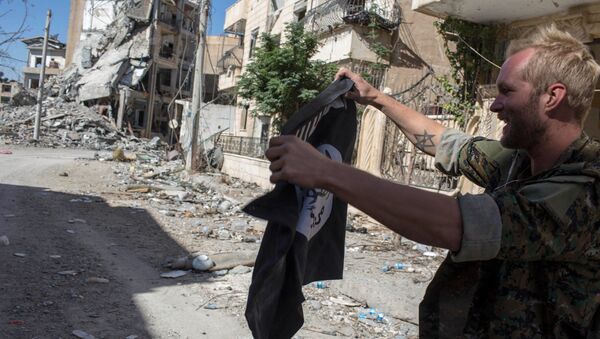 Мужчина в военной форме держит флаг ИГ (террористическая организация, запрещена в РФ) в Ракке