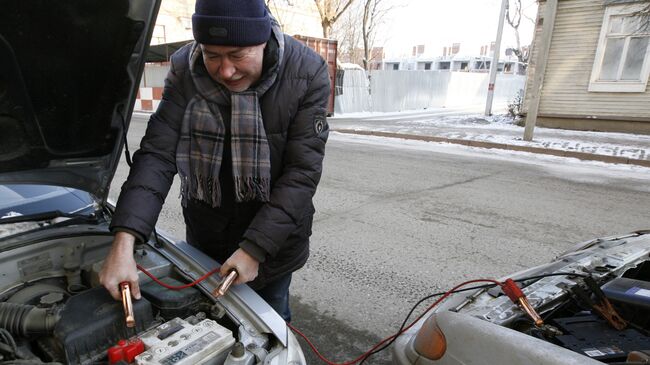 Мужчина прикуривает аккумулятор от другого автомобиля