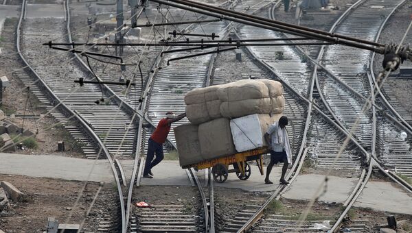 Мужчины перевозят груз через железнодорожные пути в Нью-Дели, Индия