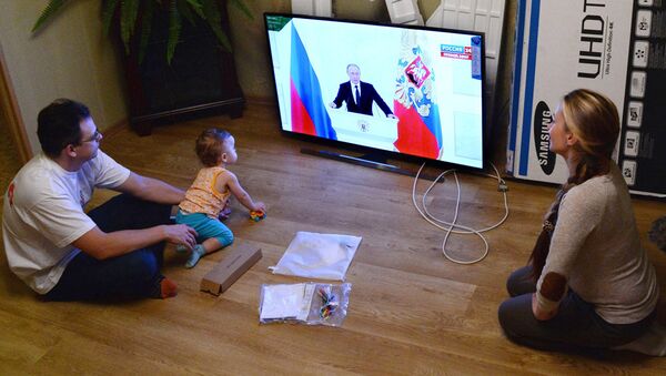 Молодая семья смотрит телевизионную трансляцию выступления президента РФ Владимира Путина