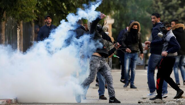 Палестинский протестующий бросает баллон со слезоточивым газом в сторону израильских военныз во время столкновений в Вифлееме на Западном берегу