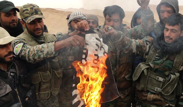 Бойцы отряда народного ополчения Соколы пустыни сжигают флаг запрещенной в России группировки ИГИЛ*, снятый с отбитой у боевиков цитадели Пальмиры