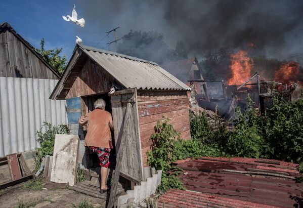 Последствия артобстрела Славянска украинскими военными. Хозяйка горящего дома входит в голубятню