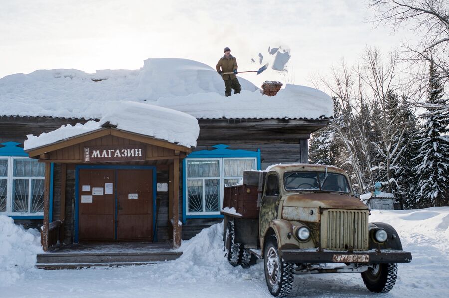 Мужчина чистит от снега крышу магазина в деревне Бобровка
