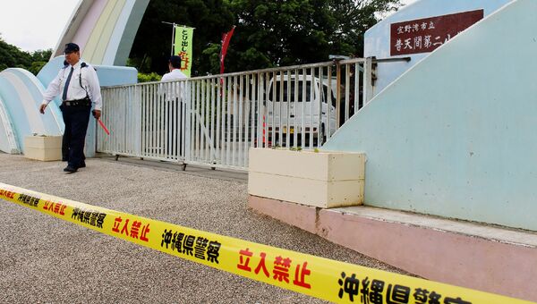 Японский полицейский у ворот начальной школы в префектуре Окинава после падения на спортивную площадку иллюминатора американского военного вертолета. 13 декабря 2017