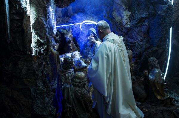 Священнослужитель, отец Мабдух помещает фигуру младенца Иисуса в рождественский вертеп во время празднования католического Рождества Христова в церкви Францисканцев Святой Земли в Каире
