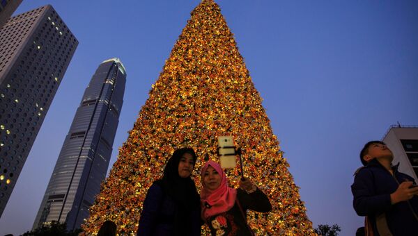 Индонезийские женщины делают селфи под гигантской елкой накануне праздника в Центральном районе Гонконга. 24 декабря 2017 года