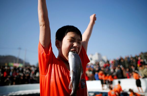 Мальчик радуется пойманной собственными руками форели во время мероприятия, посвященного ледовому фестивалю, в Хвачеоне, Южная Корея