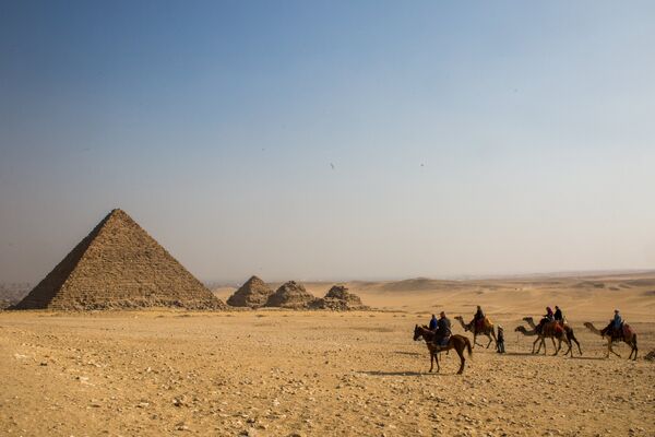 Группа туристов верхом на лошадях и верблюдах во время экскурсии к древнеегипетским пирамидам в Эль-Гизе, пригороде Каира. Слева: пирамида Микерина (Менкаура)