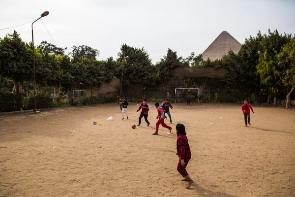 Дети играют в футбол на улиц Каира. На дальнем плане: древнеегипетская пирамида в Эль-Гизе, пригороде Каира
