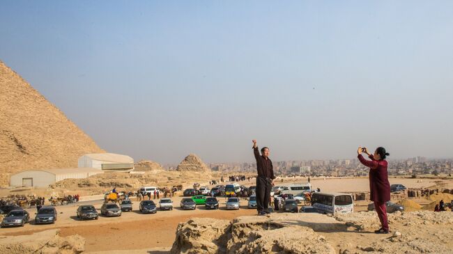 Туристы фотографируются на фоне древнеегипетских пирамид в Эль-Гизе, пригороде Каира